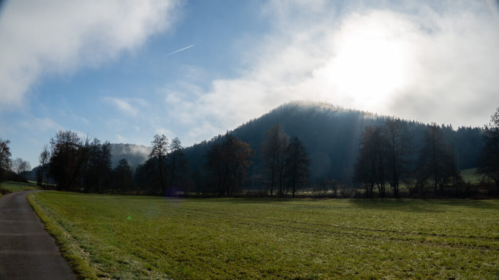Winterliches Tal mit Wiese, Waldrücken und durchscheinendem Licht auf dem Oberpfälzer Jakobsweg