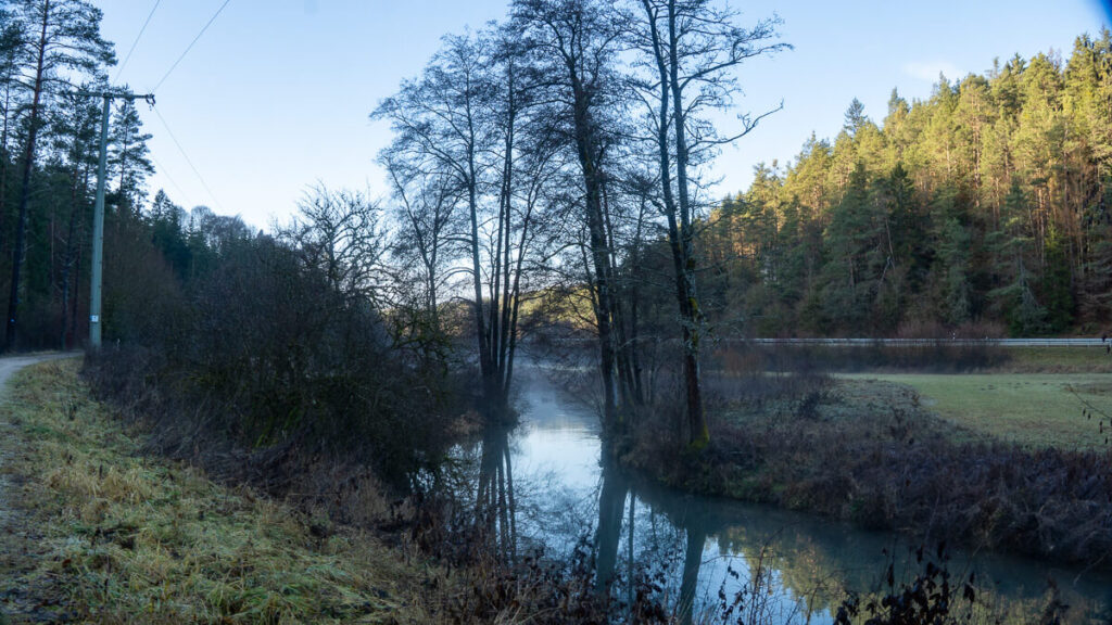 Ruhiger Flusslauf der Lauterach im winterlichen Tal mit Licht an den bewaldeten Hängen auf dem Oberpfälzer Jakobsweg