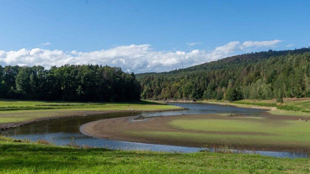 Schmaler, geschwungener Wasserlauf zwischen zwischen flachem, begrüntem Ufer